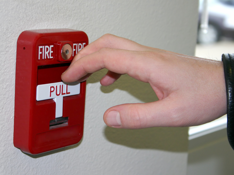 Person activating manual fire alarm, monitored for safety.